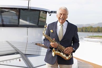 die-rhein-cruise-mit-pepe-lienhard-1.jpg Älterer Mann in Anzug mit Saxophon auf einem Boot.