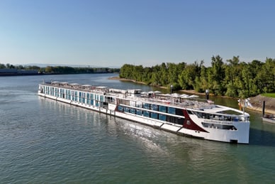 Das Flusskreuzfahrtschiff Excellence Crown liegt an einem grünen Flussufer, Gäste geniessen das Sonnendeck.