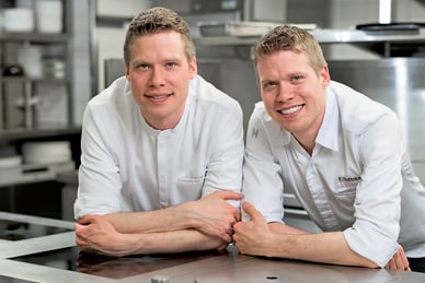 das-excellence-gourmetfestival-4.jpg Zwei Männer in weissen Kochjacken lächeln in einer professionellen Küche.
