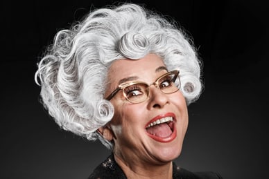 Lachende Person mit weisser Perücke und Brille.