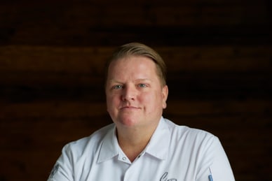 Person in weissem Kochmantel sitzt an einem Holztisch.