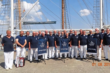 shanty-chor-in-stralsund.jpg Gruppe von Männern in Uniform vor einem Segelschiff.