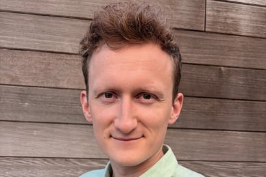 Eine Person mit grünem Hemd vor einer Holzwand.