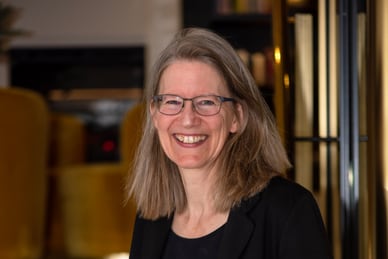 basel-amsterdam-basel-neues-aus-den-metropolen-4.jpg Lächelnde Frau mit Brille und schwarzem Blazer vor einer Treppe.