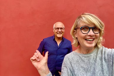 kultig-und-koestlich-mal-kurz-ins-elsass-1.jpg Zwei Personen vor einer roten Wand, eine Person hält ein Handy.