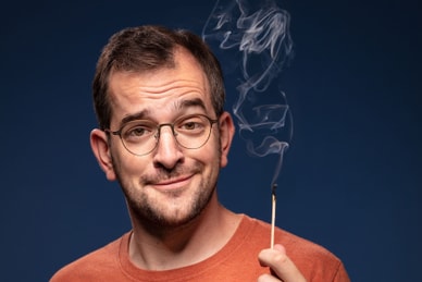 Mann mit Brille hält brennendes Streichholz.