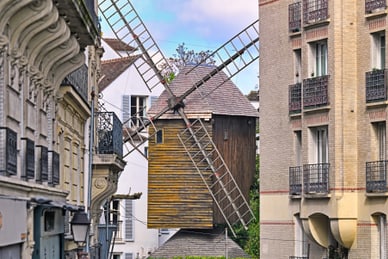 starke-frauen-grosse-geschichten-4.jpg Windmühle zwischen Gebäuden in einer Stadtlandschaft.
