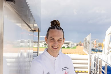 Person in weissem Outfit sitzt auf einem Bootdeck.