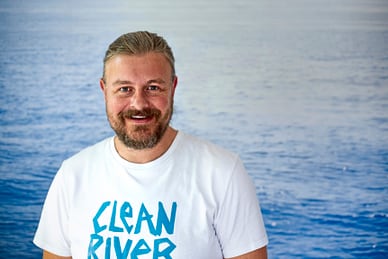 stephan-horch-vom-clean-river-project.jpg Mann im T-Shirt mit 'Clean River'-Aufdruck vor Wasserhintergrund.