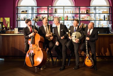 tribute-to-frank-sinatra-1.jpg Fünf Männer in Anzügen mit Musikinstrumenten vor einer Bar.