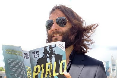 twerenbold_87563.jpg Person mit Sonnenbrille liest Buch auf einer Dachterrasse.