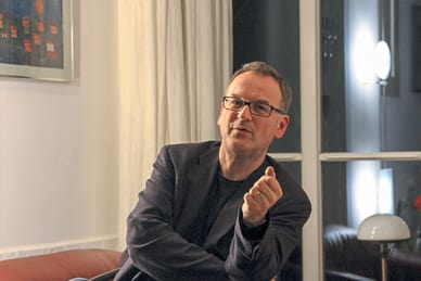 grand-tourins-donaudelta-1.jpg Person mit Brille sitzt auf Sofa und gestikuliert.