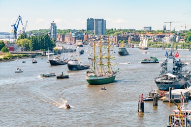hamburger-hafengeburtstag.jpg Viele Schiffe auf einem Fluss mit Stadt im Hintergrund.