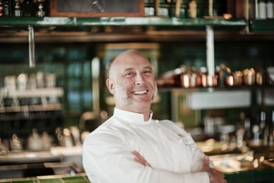 das-excellence-gourmetfestival-4.jpg Mann in weisser Kochkleidung steht in einer Restaurantküche und lächelt in die Kamera.