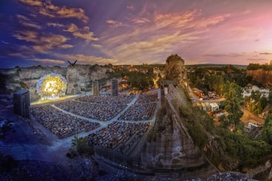tosca-im-steinbruch-st-margrethen.jpg Open-Air-Theater in Steinbruch mit beleuchteter Bühne und Publikum bei Sonnenuntergang.
