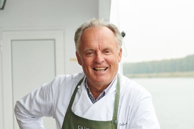 gourmetkoch-martin-dalsass.jpg Lachender Mann in Schürze auf einem Boot.