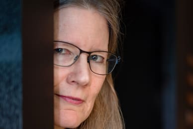 Person mit Brille schaut aus einem Türspalt hervor.