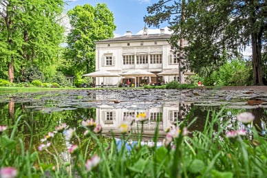 merian-gaerten.jpg Weisse Villa mit Teich und Blumen im Vordergrund.