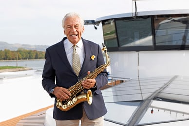 die-rhein-cruise-mit-pepe-lienhard-1.jpg Lächelnder Mann hält Saxophon auf Boot.