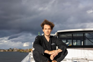 das-excellence-gourmetfestival-4.jpg Person in schwarzer Kleidung sitzt auf einem Boot, mit bewölktem Himmel im Hintergrund.