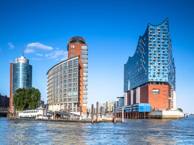 Elbphilharmonie in Hamburg mit Glasaufbau auf rotem Backsteinbau, daneben moderne Hafenarchitektur und vertäute Boote.