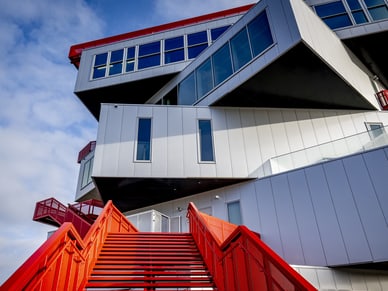 Modernes Gebäude mit roten Treppen und kantiger Architektur gegen blauen Himmel.
