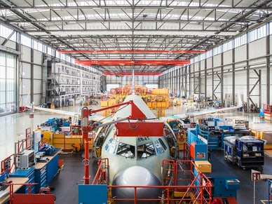 Grosser Flugzeugrumpf der A320-Familie in einer Montagehalle mit gelben Arbeitsstationen und roten Kränen.
