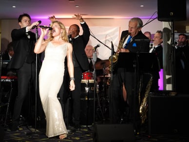 Frau in weissem Kleid singt auf Bühne mit Band im Hintergrund.
