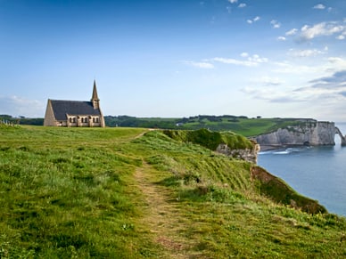 Steinerne Kapelle auf grüner Anhöhe über den Kreidefelsen von Étretat, Normandie, mit Blick aufs Meer.