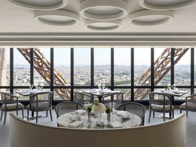 Elegant gedeckte Tische im Restaurant Le Jules Verne mit Blick auf die Stahlkonstruktion des Eiffelturms und Paris.