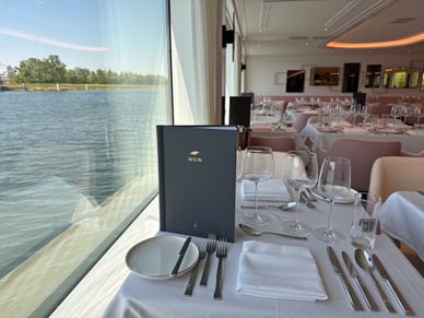 Elegant gedeckter Tisch im Bordrestaurant der Excellence Crown mit Blick durch grosse Fenster auf den Fluss.