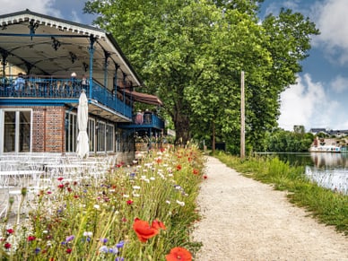 Das Maison Fournaise in Chatou mit Terrasse, Blumenwiese und Blick auf die Seine unter blauem Himmel.