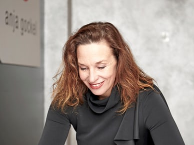 Anja Gockel sitzt konzentriert an einem Tisch und arbeitet mit Stift, Papier und Stoffproben an neuen Modeentwürfen.