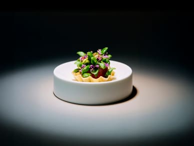 Feines Essen in weissem Teller auf dunklem Hintergrund ausgeleuchtet.