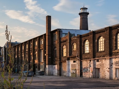 Verwittertes Backsteingebäude mit Graffiti und Schornstein des Heliosturms in Köln unter blauem Himmel.