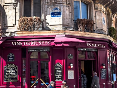 Zwei ältere Personen sitzen an einem Aussentisch des Café des Musées in Paris und unterhalten sich bei Getränken.