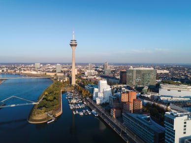 Luftaufnahme von Düsseldorf mit dem Rheinturm, dem Medienhafen und einer Brücke über den Rhein bei Sonnenschein.