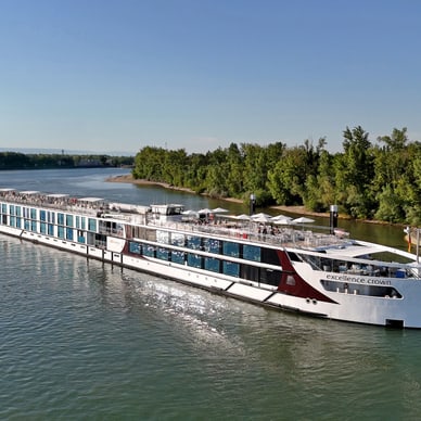 Flusskreuzfahrtschiff fährt auf einem Fluss, mit Bäumen am Ufer.