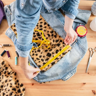 Person misst Stoff auf Jeansjacke mit Massband.