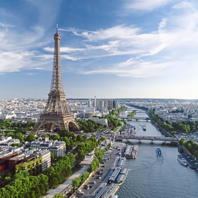 Vogelperspektive auf Paris mit Eiffelturm, Seine und mehreren Brücken unter blauem Himmel.