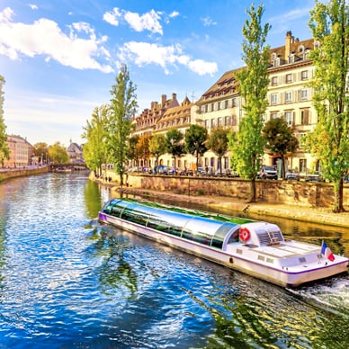 Fluss mit Touristenboot und Häusern im Hintergrund.