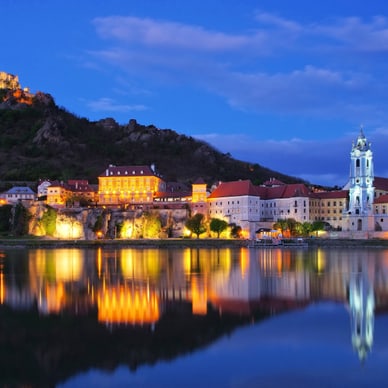 Abendliche Flusslandschaft mit beleuchteten Gebäuden und Kirche.