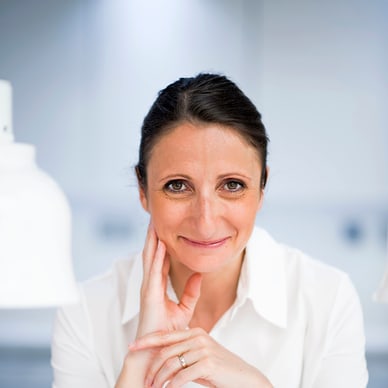 Frau in weissem Hemd lächelt in hellem Raum.