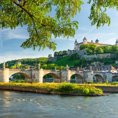 Alte Steinbrücke über Fluss mit Festung im Hintergrund.