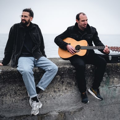 Zwei Männer an der Küste, einer spielt Gitarre.