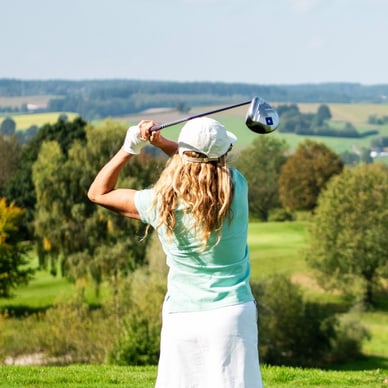Frau schwingt Golfschläger auf grünem Golfplatz.