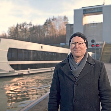 Mann steht vor einem modernen Flusskreuzfahrtschiff und einer Schleusenanlage.