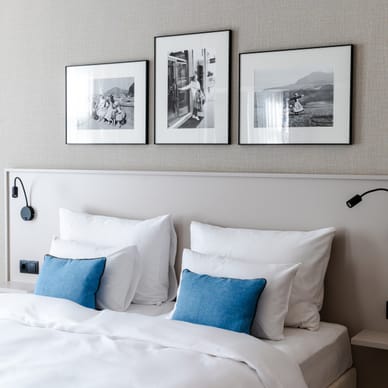 Modernes Schlafzimmer mit Doppelbett, blauen Kissen und drei Schwarzweissbildern an der Wand darüber.