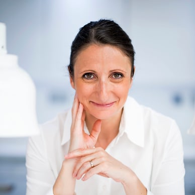 Frau in weissem Hemd lächelt in hellem Raum.