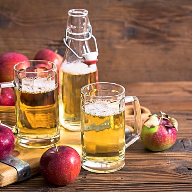 Frische Äpfel und Apfelwein in Gläsern auf Holztisch.